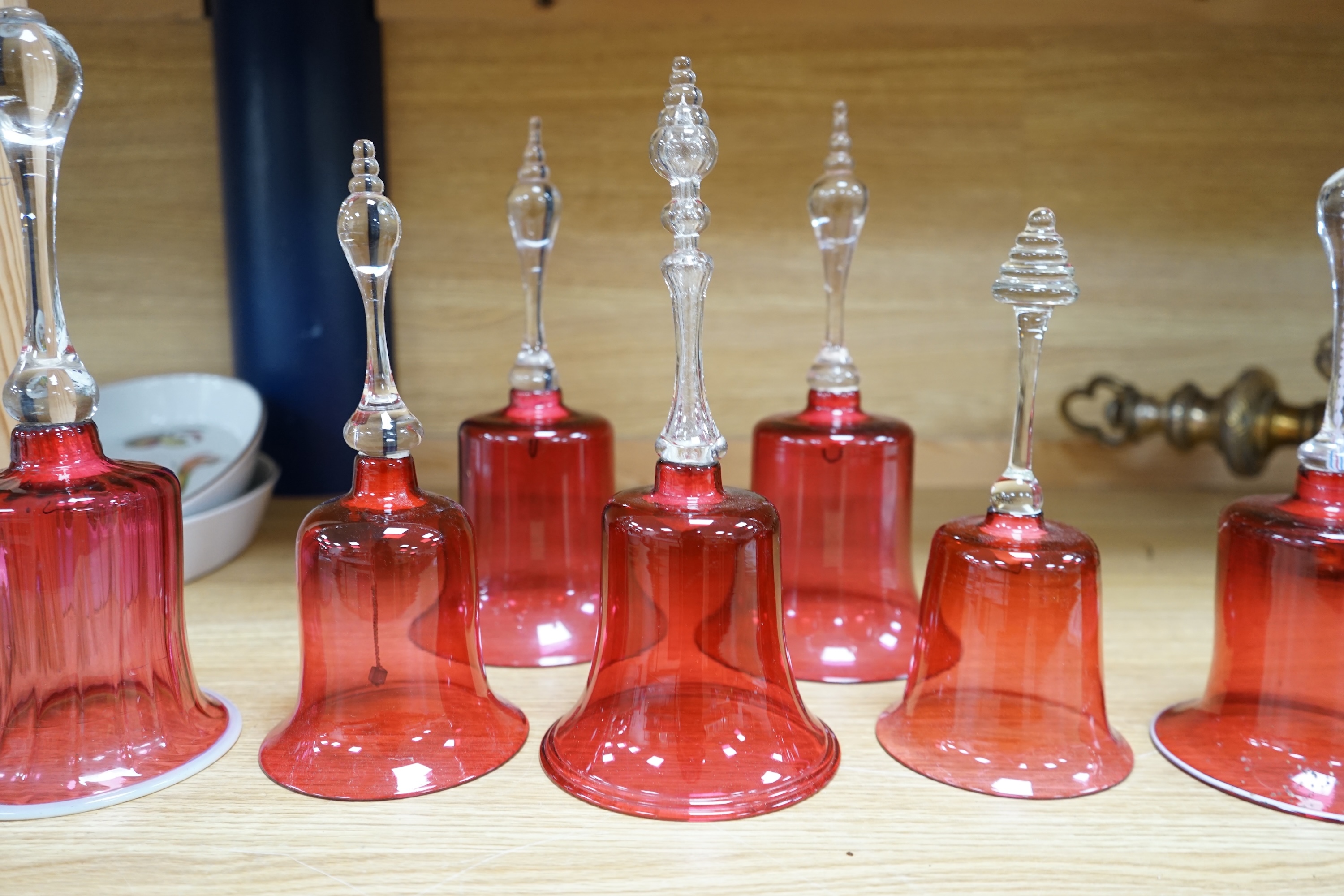 Seven 19th century cranberry glass hand bells, various sizes, largest 30.5cm high. Condition - fair